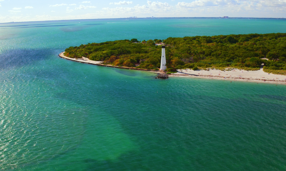 Birds eye view of a lighthouse on the southern tip of Miami, surrounded by green-blue waters